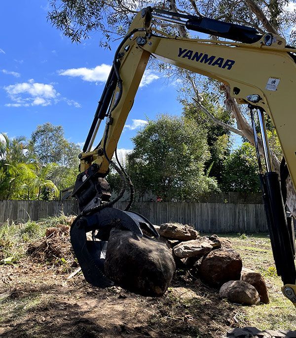A Yanmar Excavator is Digging a Pile of Rocks in a Yard — Tallow Tree Services Pty Ltd in Bangalow, NSW
