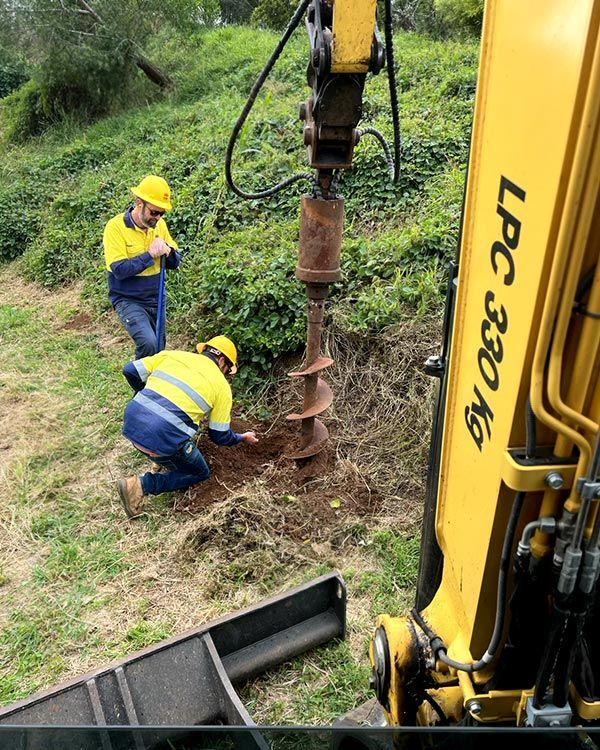 Two Men Are Working on a Hole in the Ground Next to a Yellow Excavator — Tallow Tree Services Pty Ltd in Bangalow, NSW