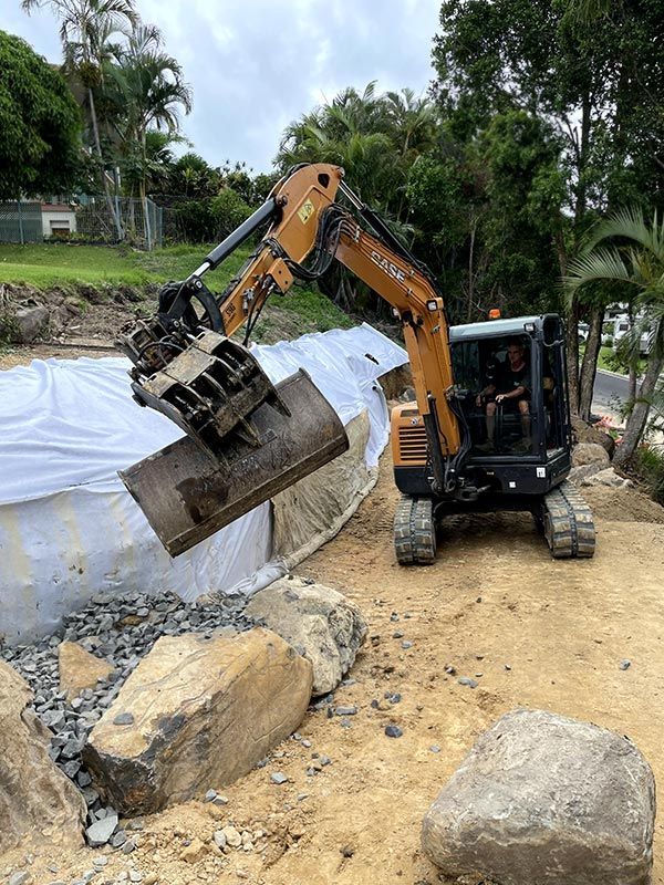 A Bulldozer is Moving Rocks on a Dirt Road — Tallow Tree Services Pty Ltd in Bangalow, NSW