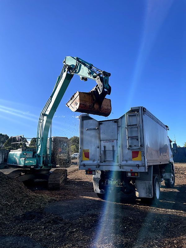 An Excavator is Loading a Dump Truck With Dirt — Tallow Tree Services Pty Ltd in Bangalow, NSW