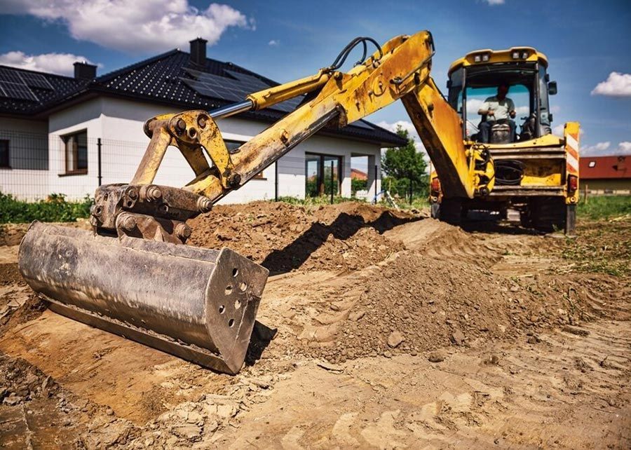 A Yellow Excavator is Moving Dirt on a Construction Site in Front of a House — Tallow Tree Services Pty Ltd in Bangalow, NSW
