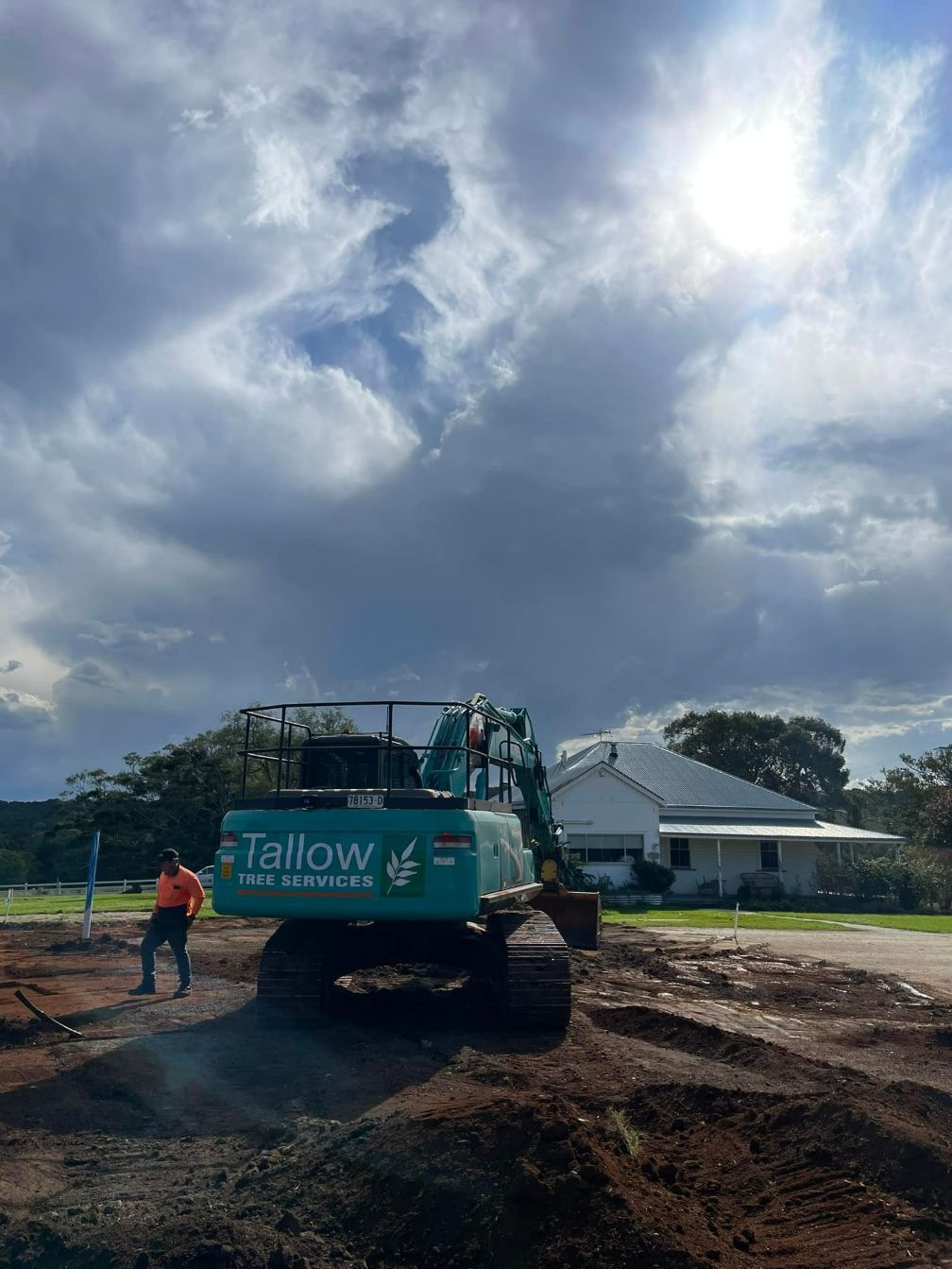A Blue Excavator is Sitting on Top of a Dirt Field in Front of a House — Tallow Tree Services Pty Ltd in Kyogle, NSW
