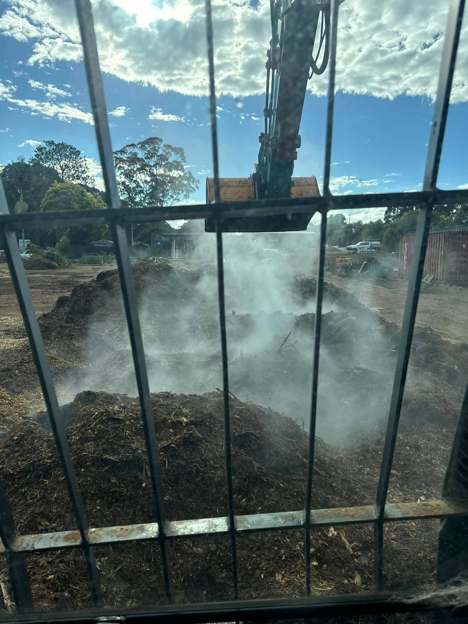 A Large Pile of Dirt is Behind a Fence and Smoke is Coming Out of It — Tallow Tree Services Pty Ltd in Alstonville, NSW