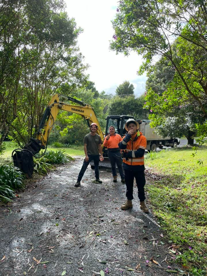 A Group of Men Are Standing Next to a Yellow Excavator on a Dirt Road — Tallow Tree Services Pty Ltd in Evans Head, NSW