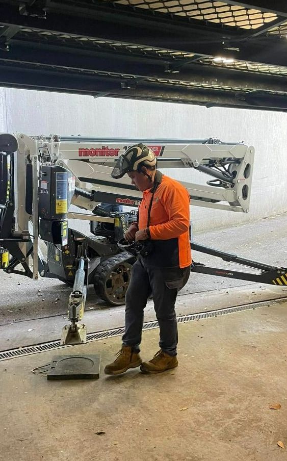A Man is Standing Next to a Crane in a Garage — Tallow Tree Services Pty Ltd in Lismore, NSW