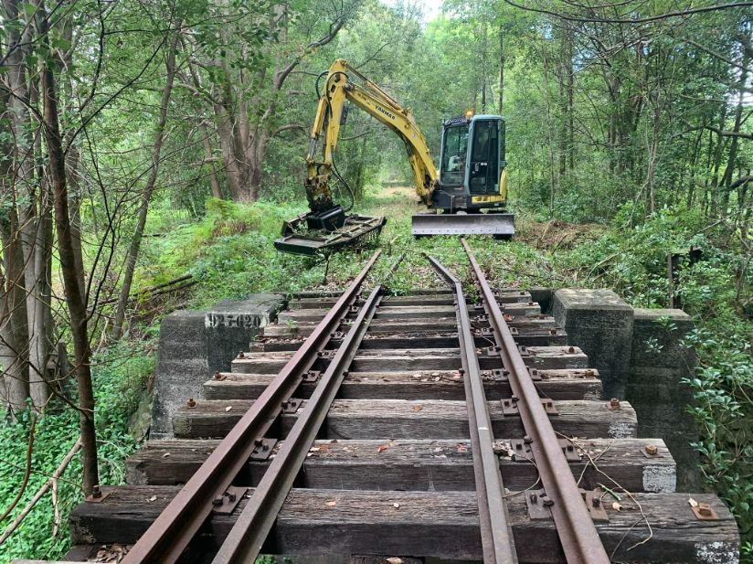 A Yellow Excavator is Working on Train Tracks in the Woods — Tallow Tree Services Pty Ltd in Alstonville, NSW