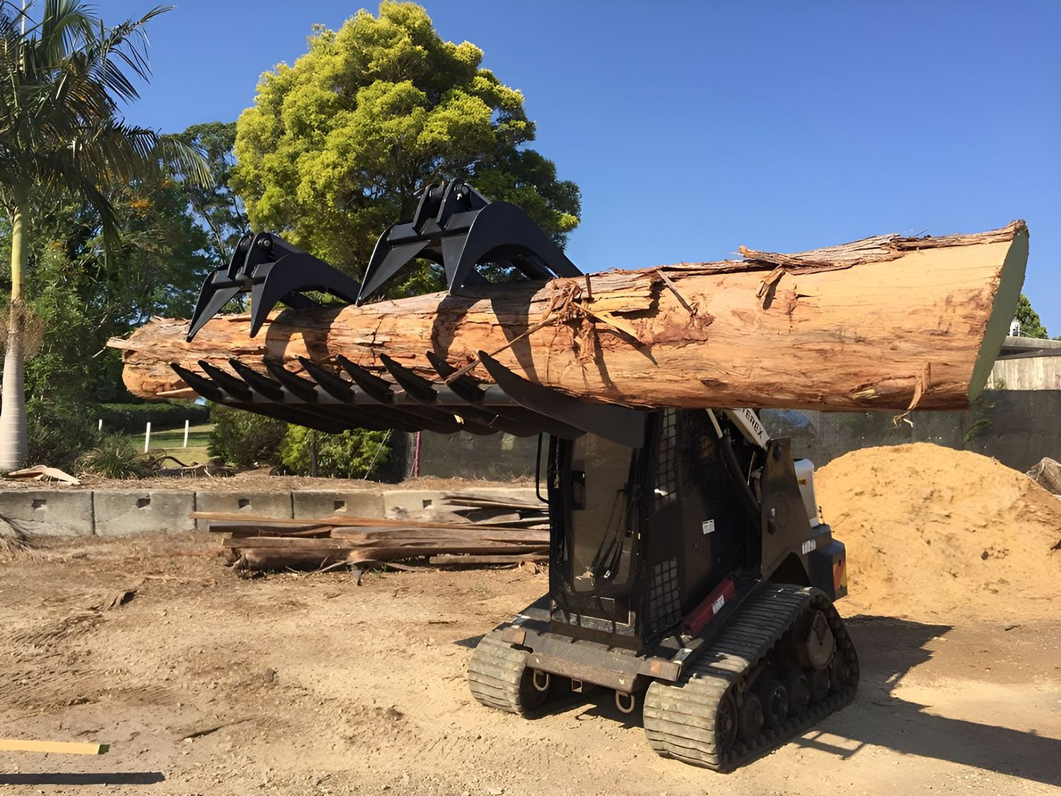 Mini Skid Steer with Claw Attachment Lifting a Large Log