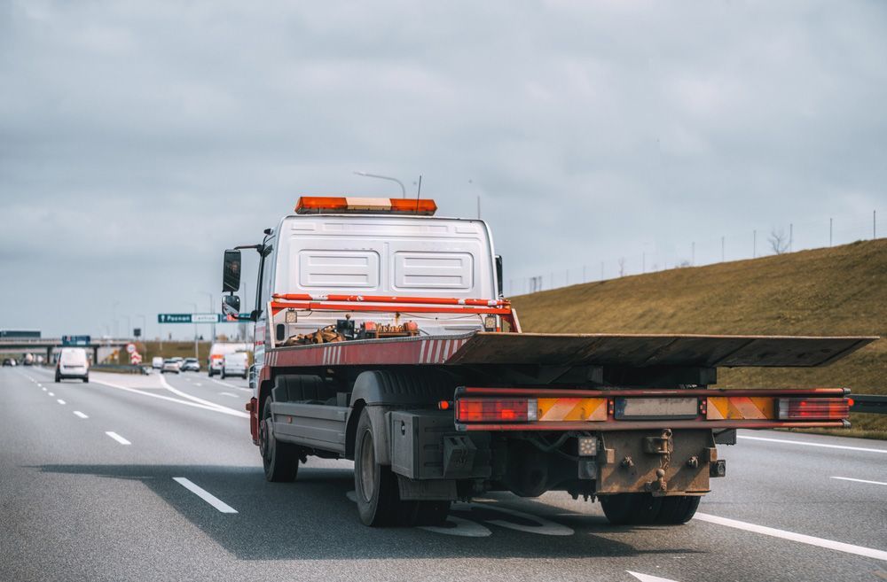 A Tow Truck With a Flat Bed is Driving Down a Highway — Tallow Tree Services Pty Ltd in Tweed Heads, NSW