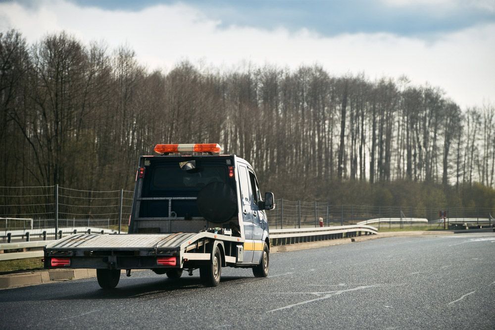 A Tow Truck is Driving Down a Highway Next to a Forest — Tallow Tree Services Pty Ltd in Ballina, NSW