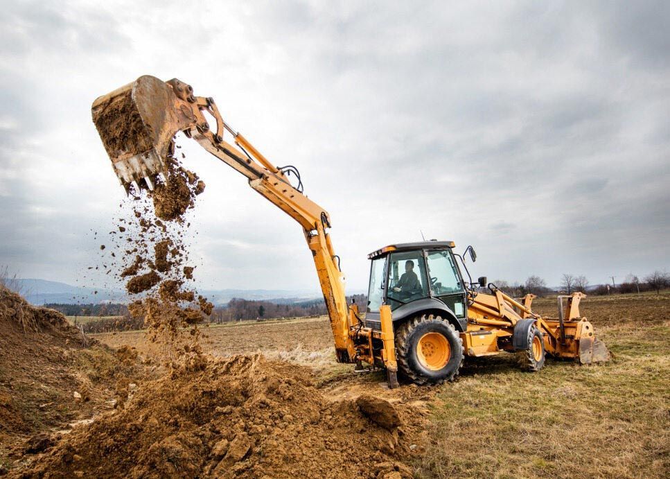 A Bulldozer is Digging a Hole in a Field — Tallow Tree Services Pty Ltd in Bangalow, NSW