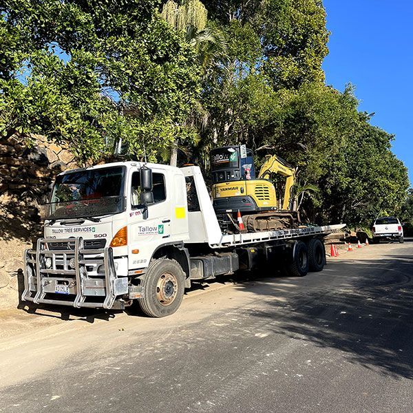 A Tow Truck is Parked on the Side of the Road Next to a Yellow Excavator — Tallow Tree Services Pty Ltd in Byron Bay, NSW