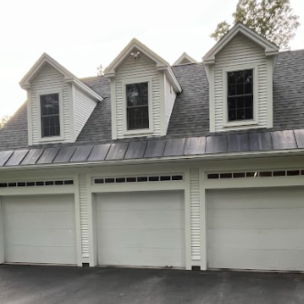 White three-car garage with three dormers, black roof, and dark driveway.