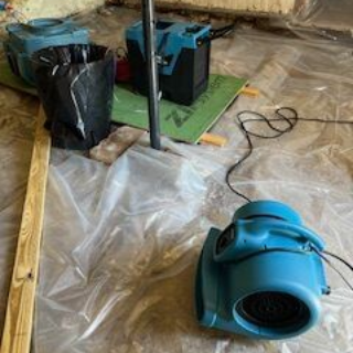 Blue industrial fans and other equipment sit on plastic sheeting in a basement.