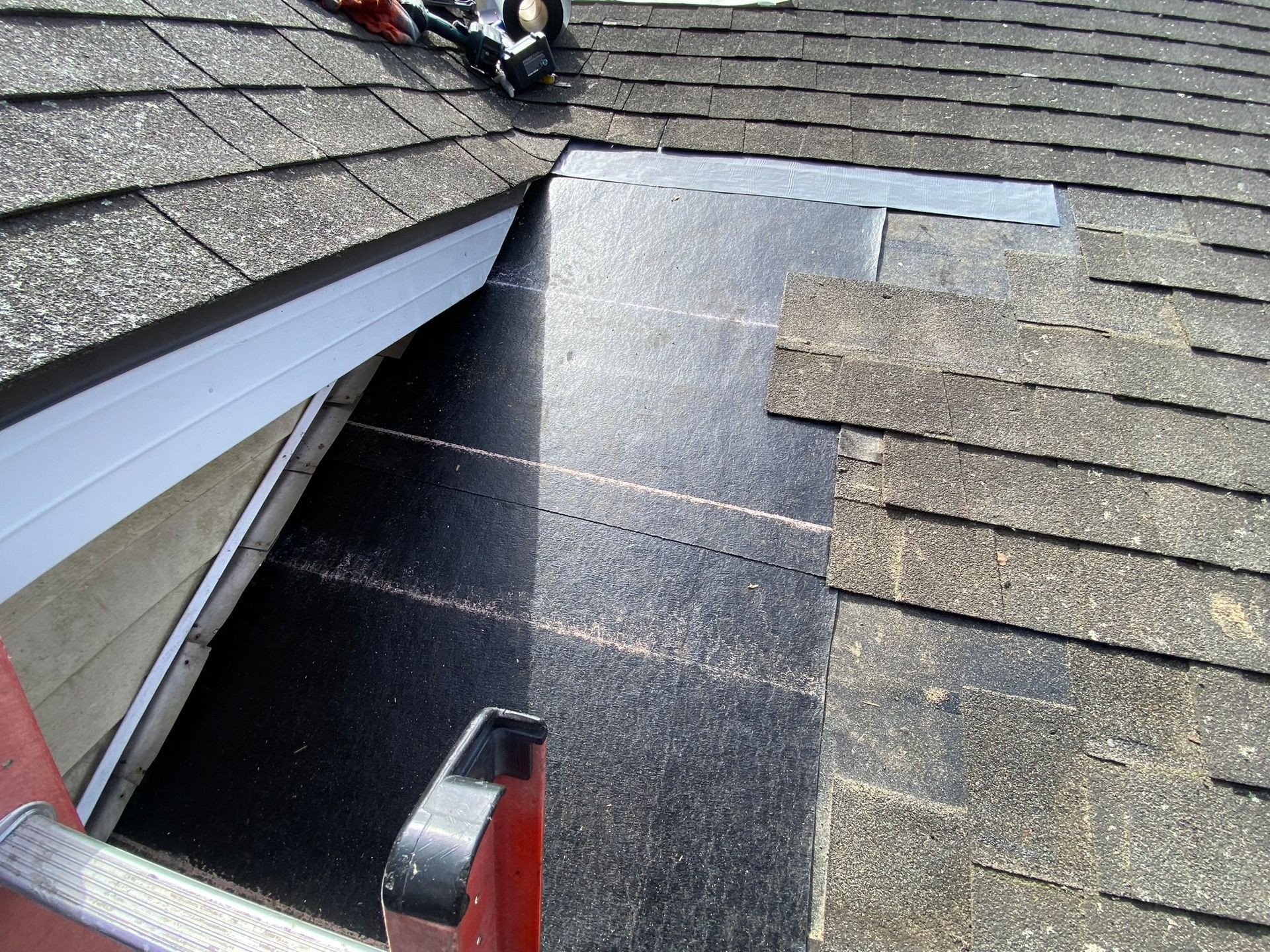 A ladder is sitting on top of a roof next to a window.