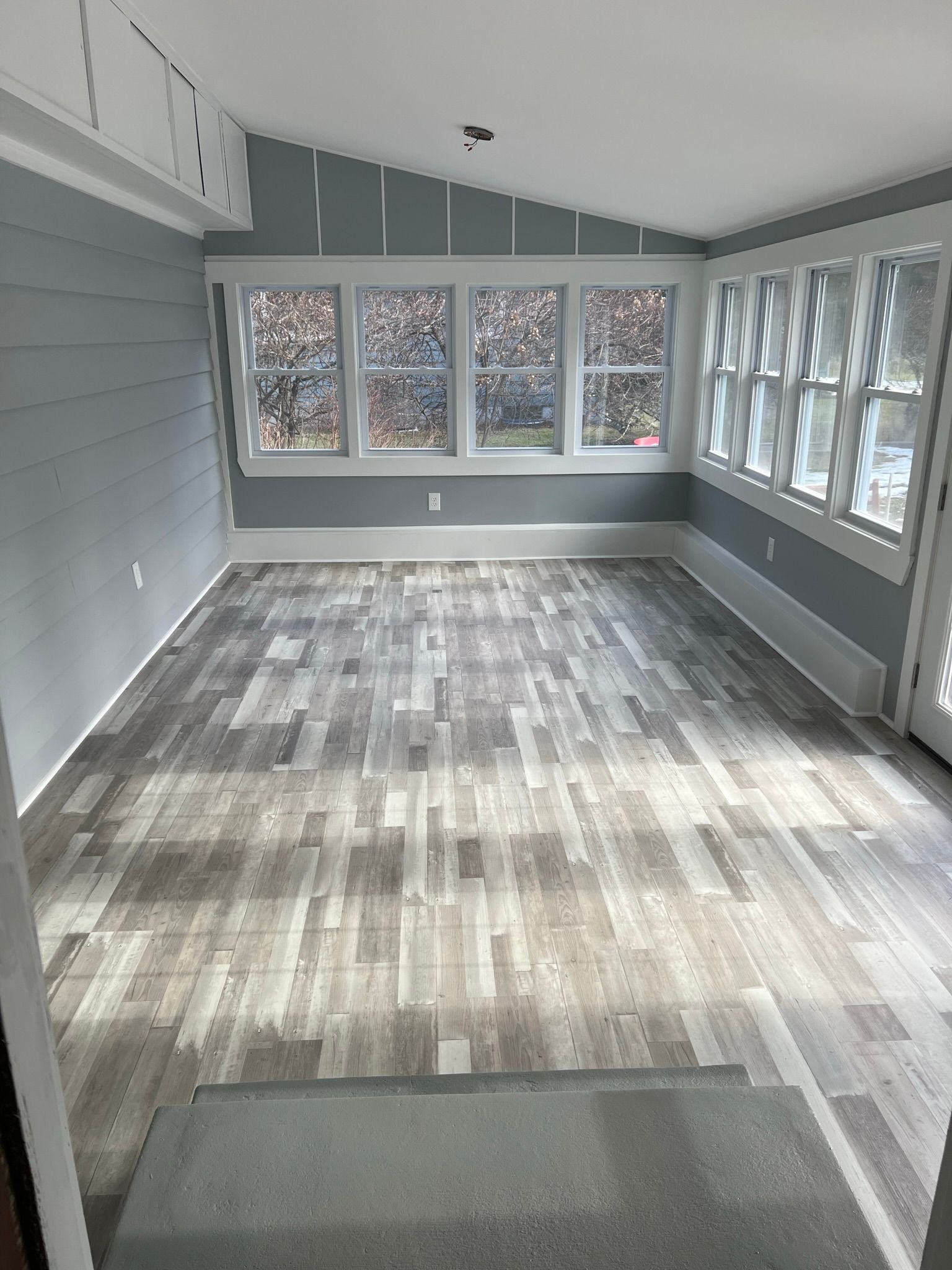 An empty room with a wooden floor and lots of windows.