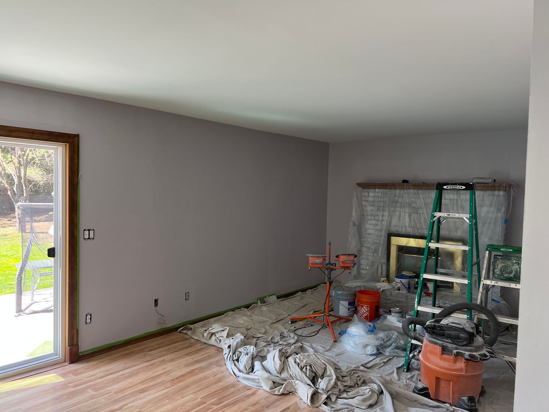A living room is being painted with a vacuum cleaner and ladder.