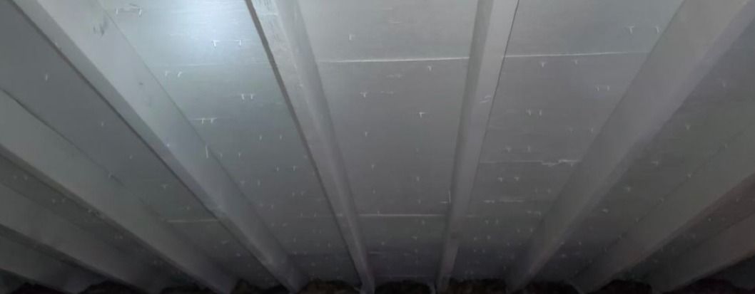 A close up of a ceiling with a fan in the background.