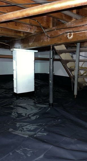 A basement with a black tarp on the floor and wooden beams.