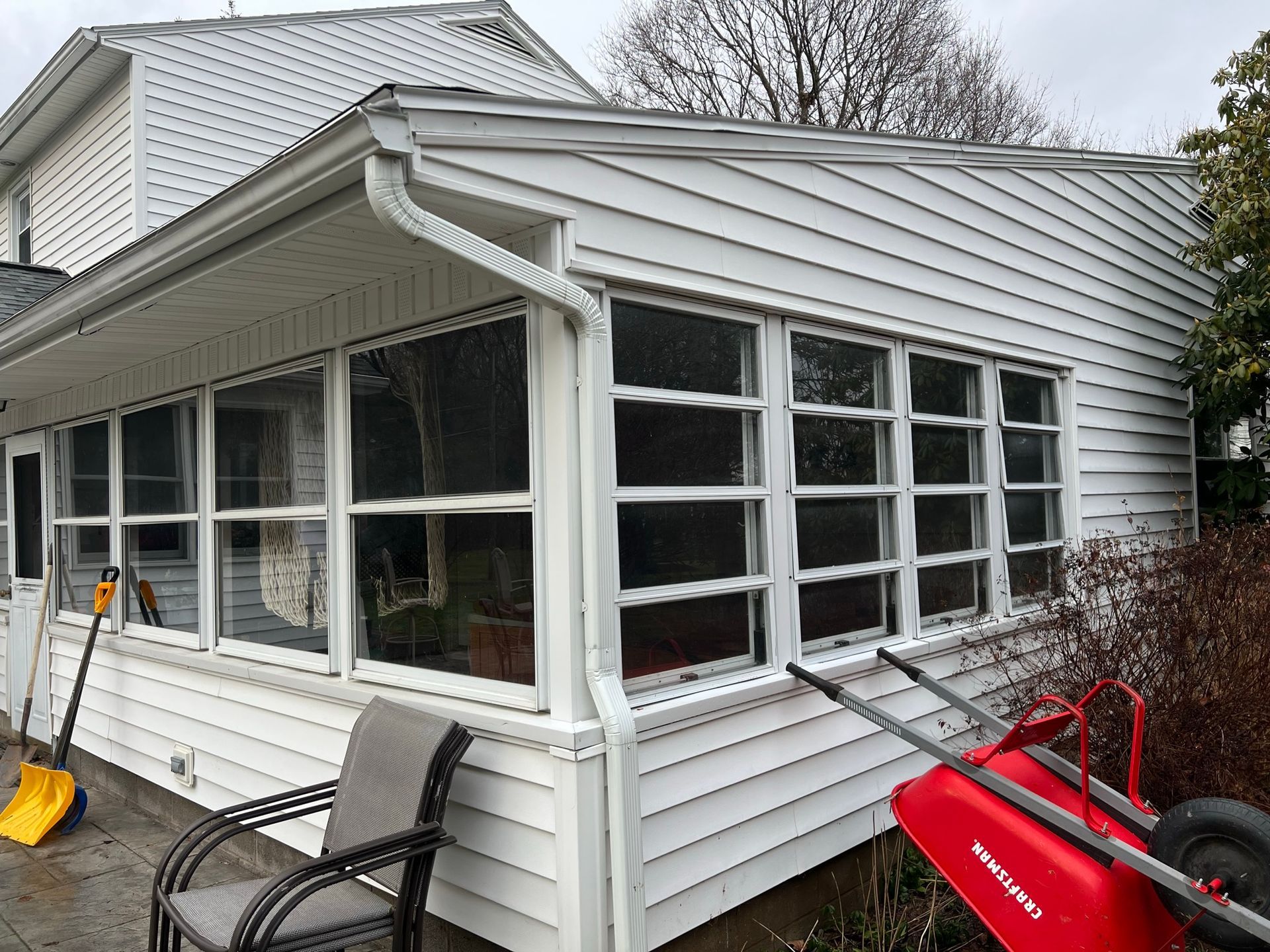 A red wheelbarrow is parked in front of a white house.