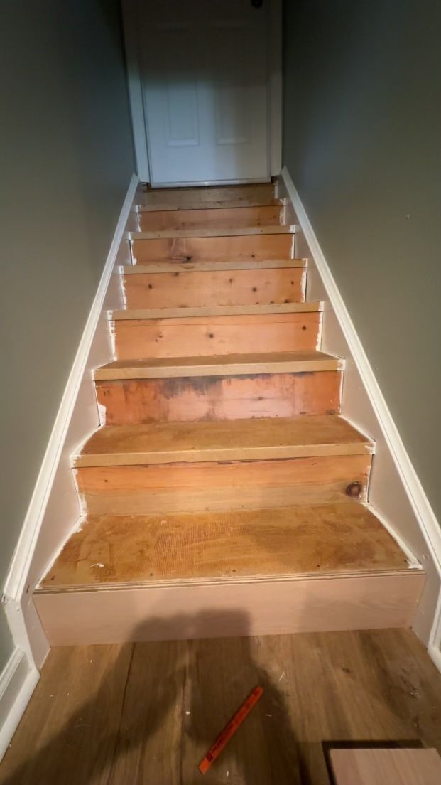A row of wooden stairs leading up to a door in a hallway.