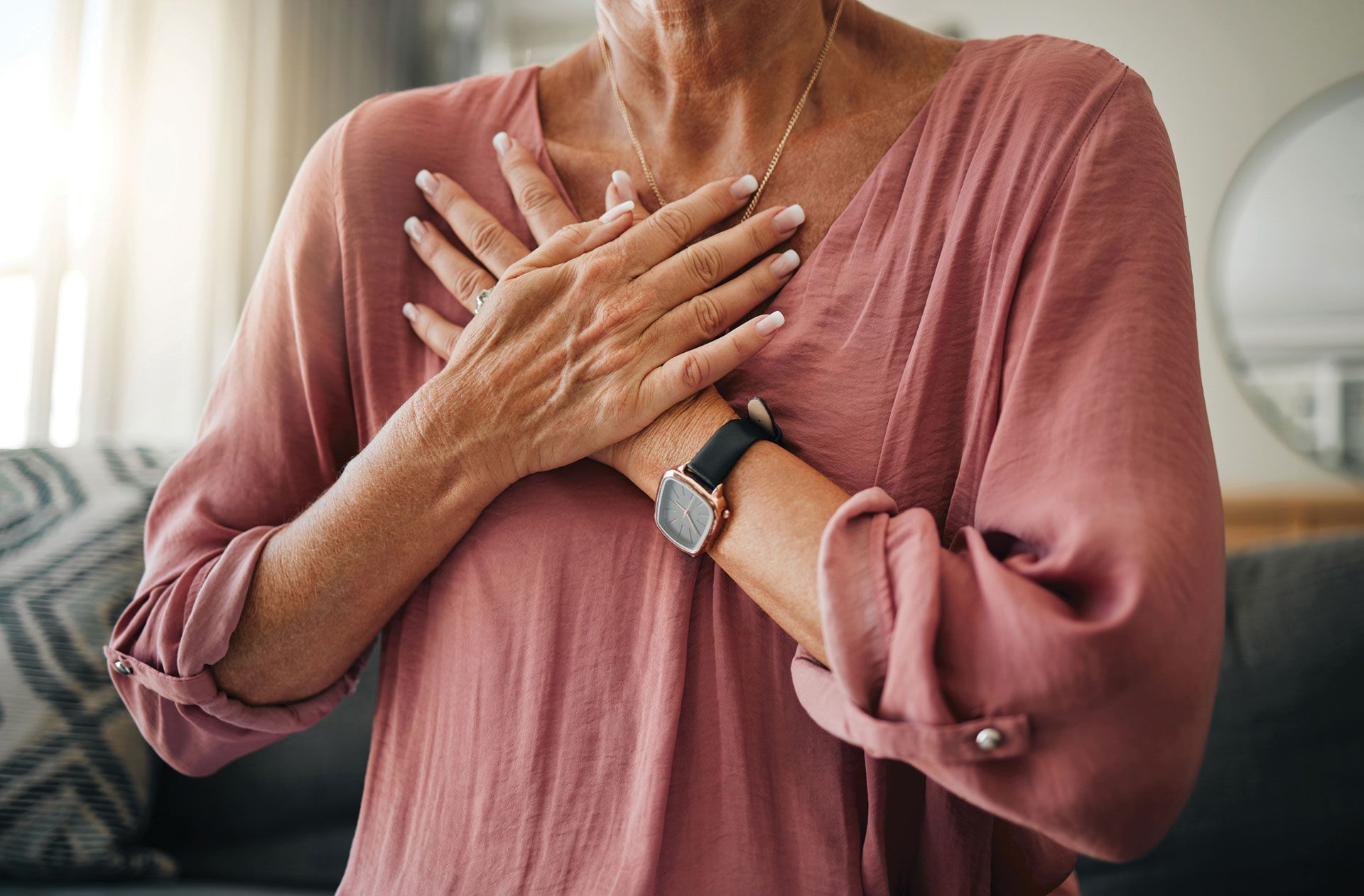 A woman in a pink shirt is holding her hands to her chest.