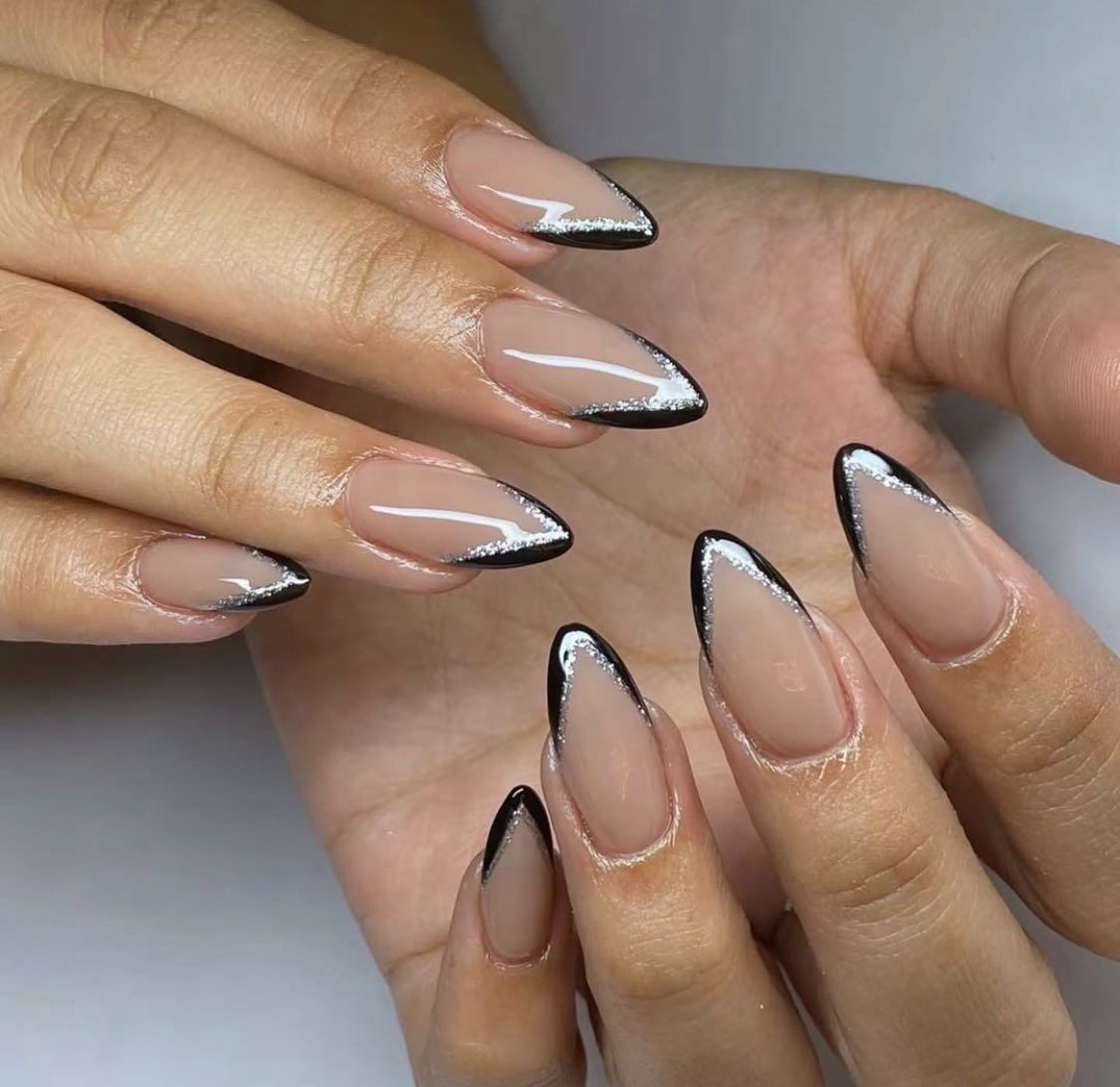 Manicured almond-shaped nails with a nude base and thin black and silver glitter French tips.