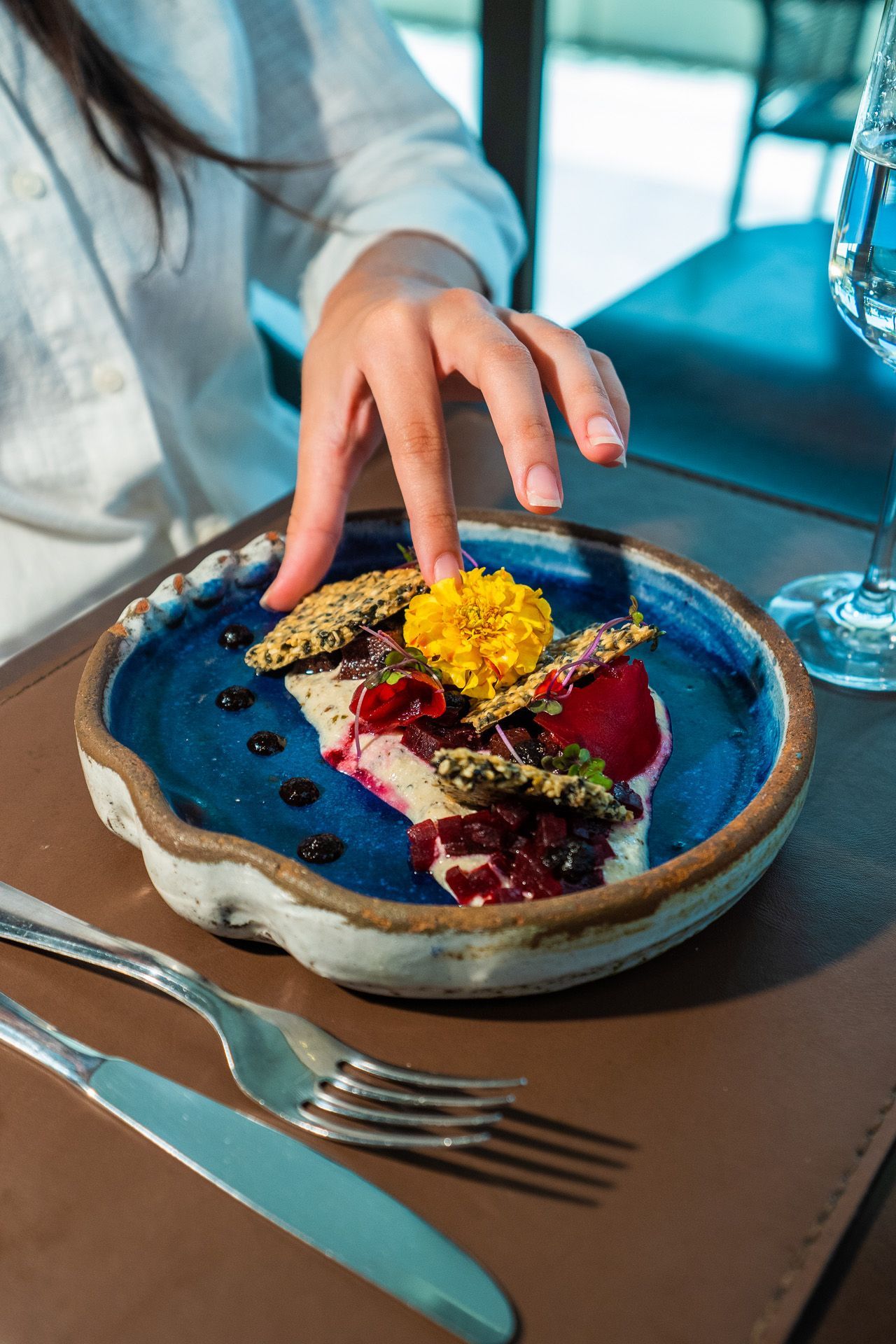 Mão de pessoa alcançando um prato colorido com base azul, guarnição amarela e molhos escuros.