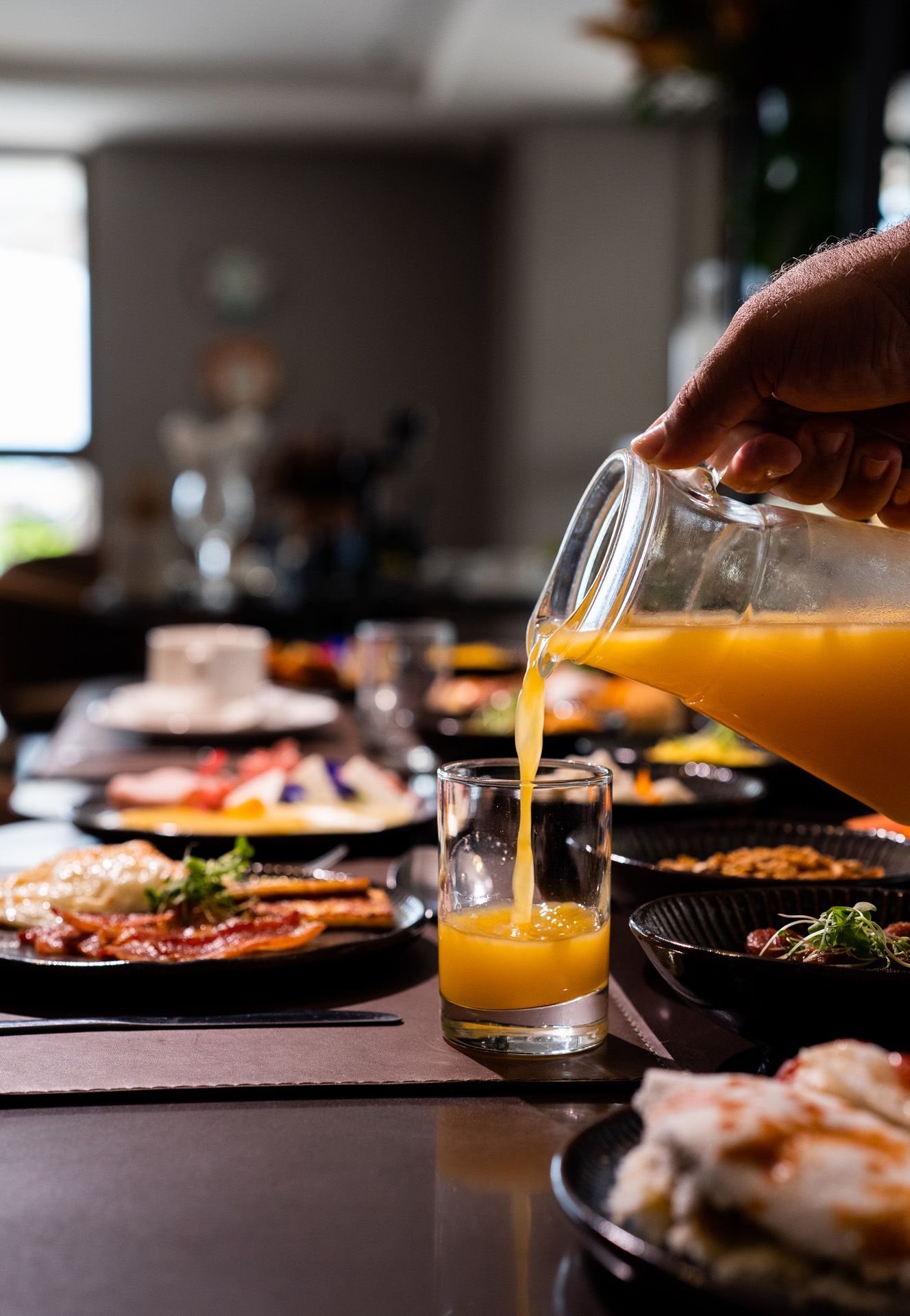 Servir suco de laranja em um copo à mesa do café da manhã, acompanhado de diversos pratos.