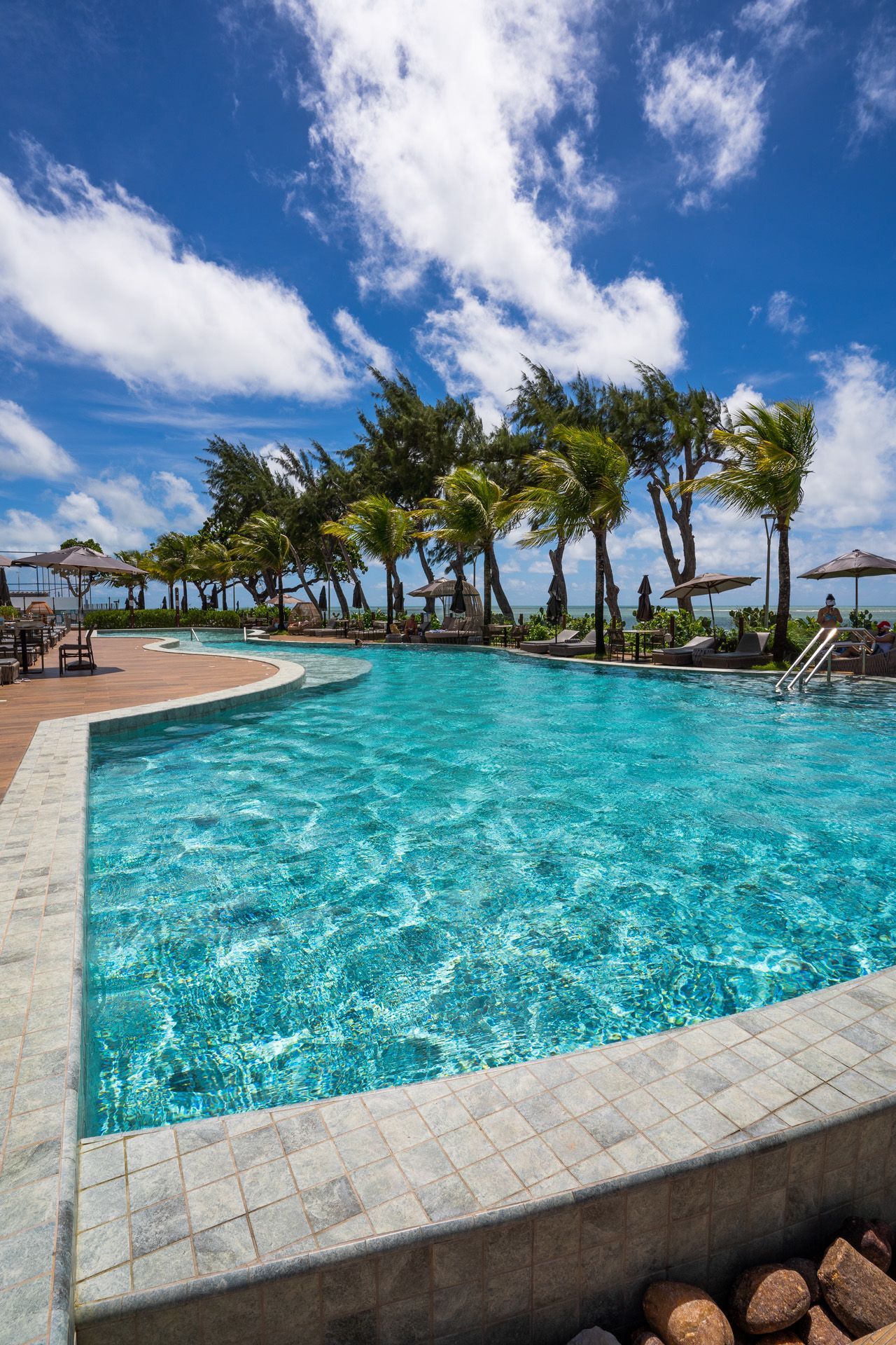 Piscina com água turquesa, palmeiras e céu azul com nuvens.