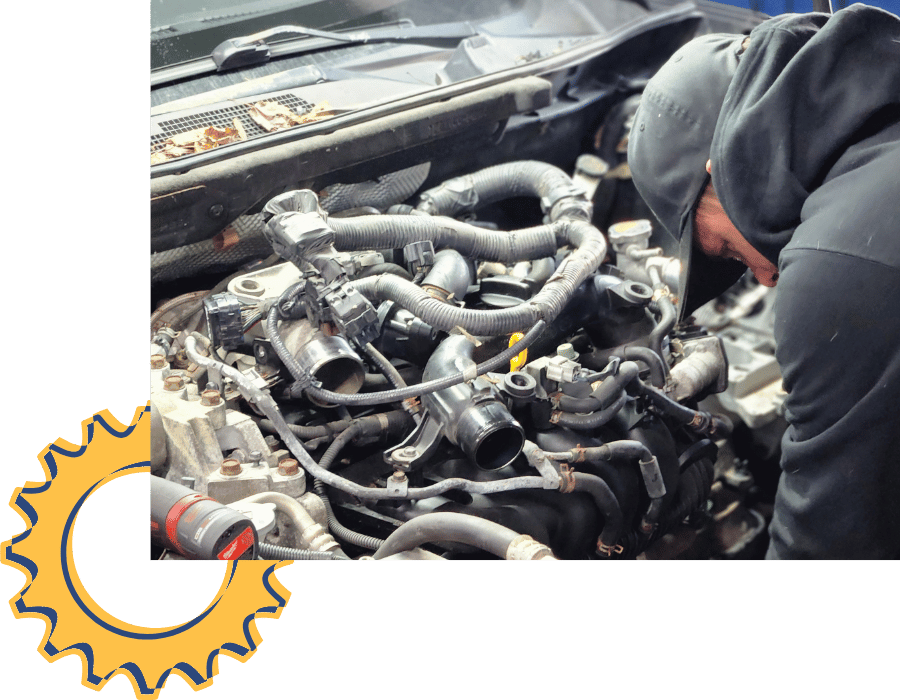 Technician working under the hood of a white pickup truck during engine repair.