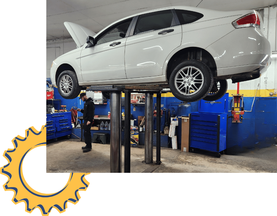 White Ford sedan raised on hydraulic lift inside auto repair shop.
