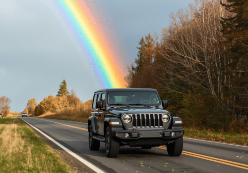 Jeep driving on a rural road with a bright rainbow overhead and trees lining the roadside.