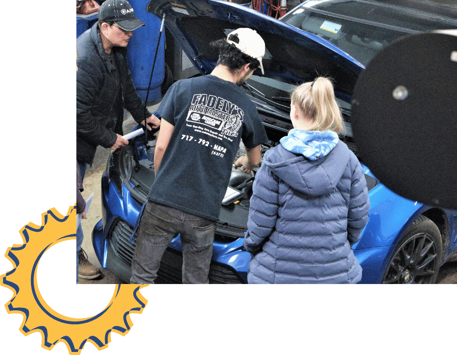 Technician explaining engine repairs to customers under open hood at Fadely&rsquo;s Auto Masters.