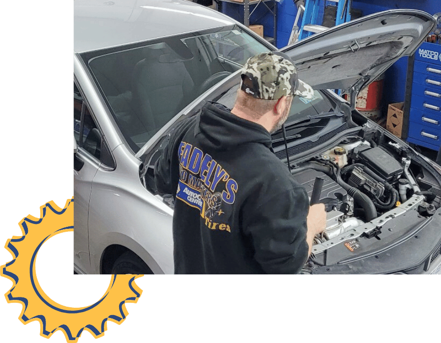 Technician inspecting engine bay of silver vehicle during maintenance service.