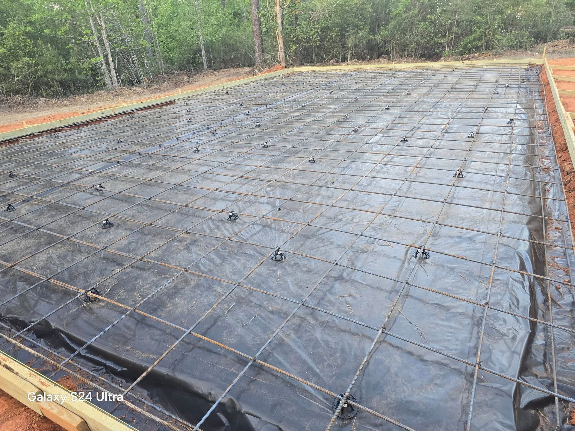 Construction site: Rebar grid over black sheeting within wooden frame, ready for concrete pour.
