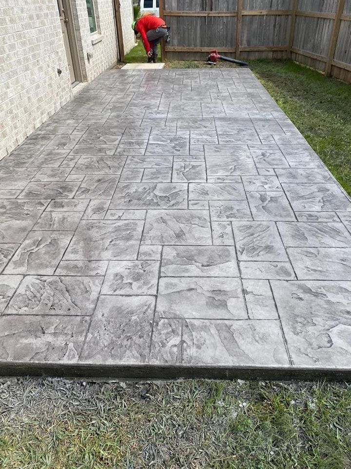 Stamped concrete patio with a person working near a brick wall and fence.