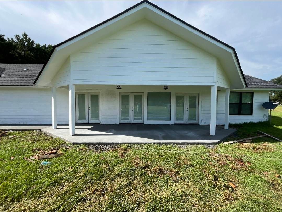 White house exterior with porch, French doors, concrete patio, and green grass.