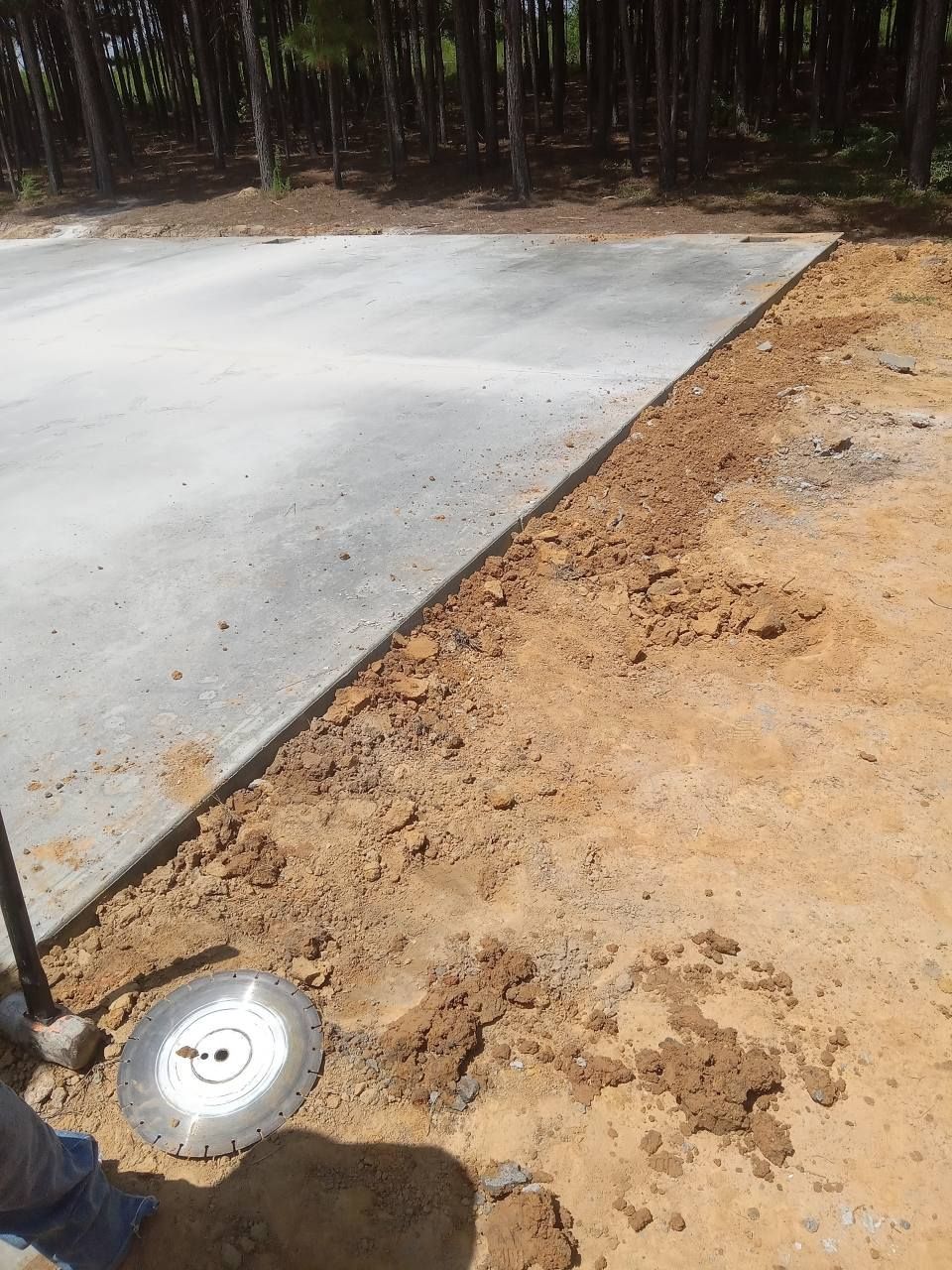 Concrete slab edge next to dirt, saw blade visible, with trees in the background.