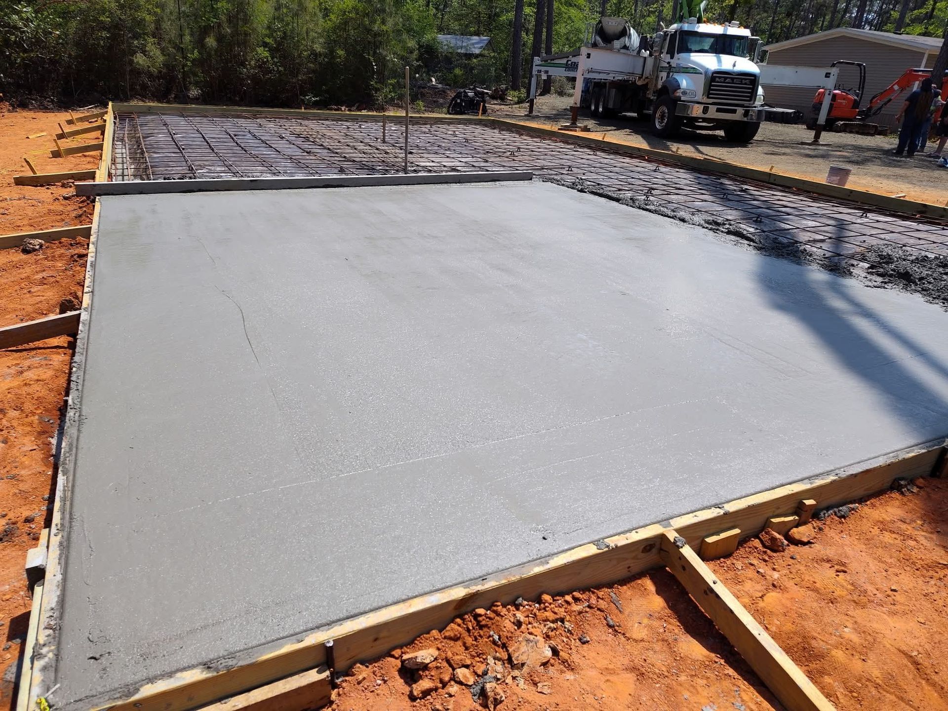 Freshly poured concrete slab in wooden frame, with concrete truck in the background.