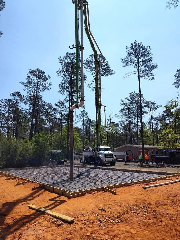 Concrete being poured via pump truck onto a prepared construction site in a wooded area.