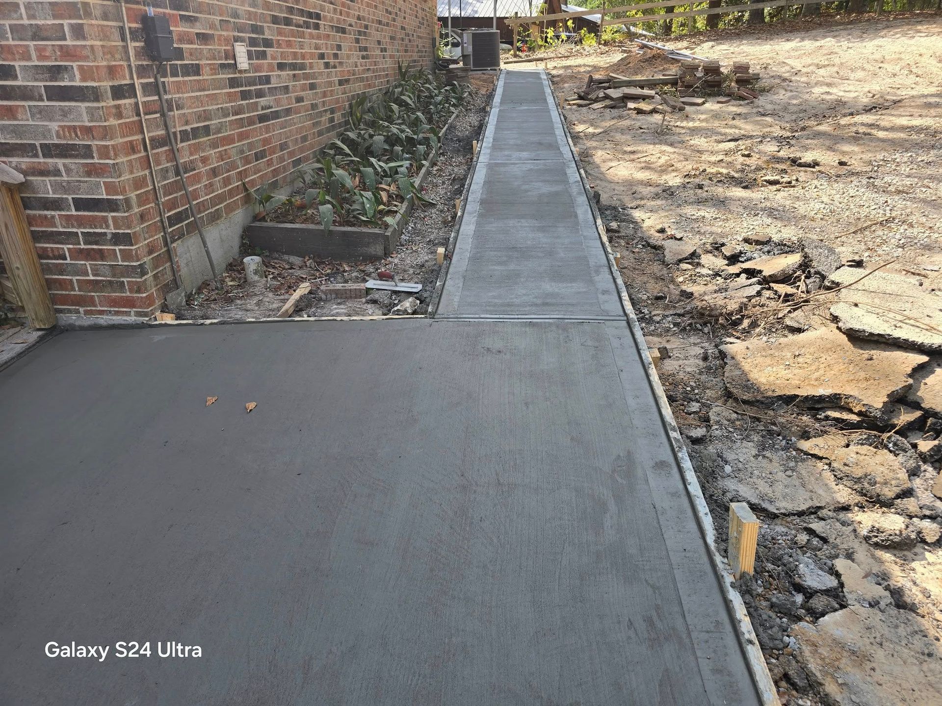 Freshly poured concrete sidewalk next to a brick building. Construction debris visible.
