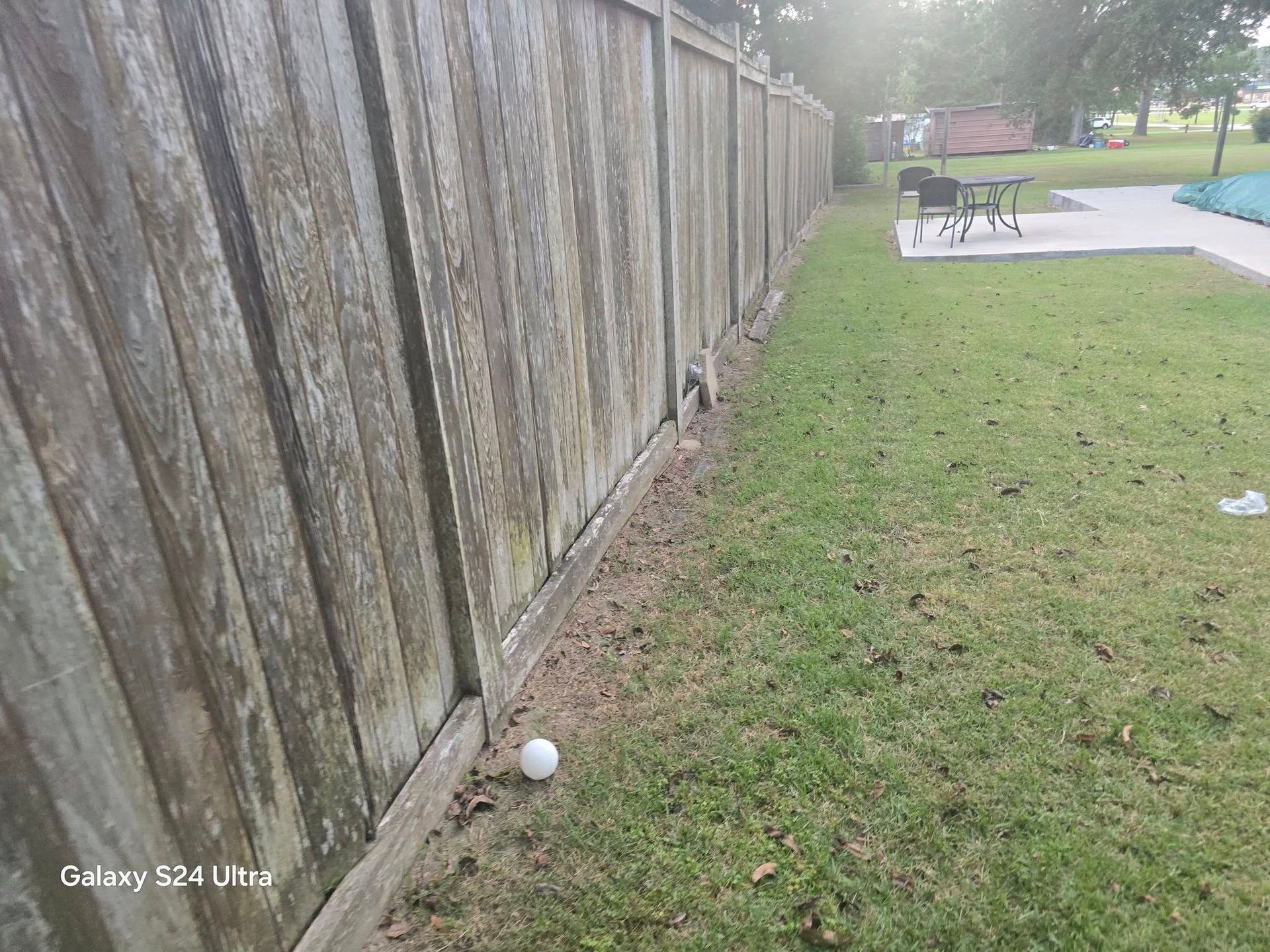 Wooden fence along a grassy yard with a golf ball in the foreground and pool in the distance.