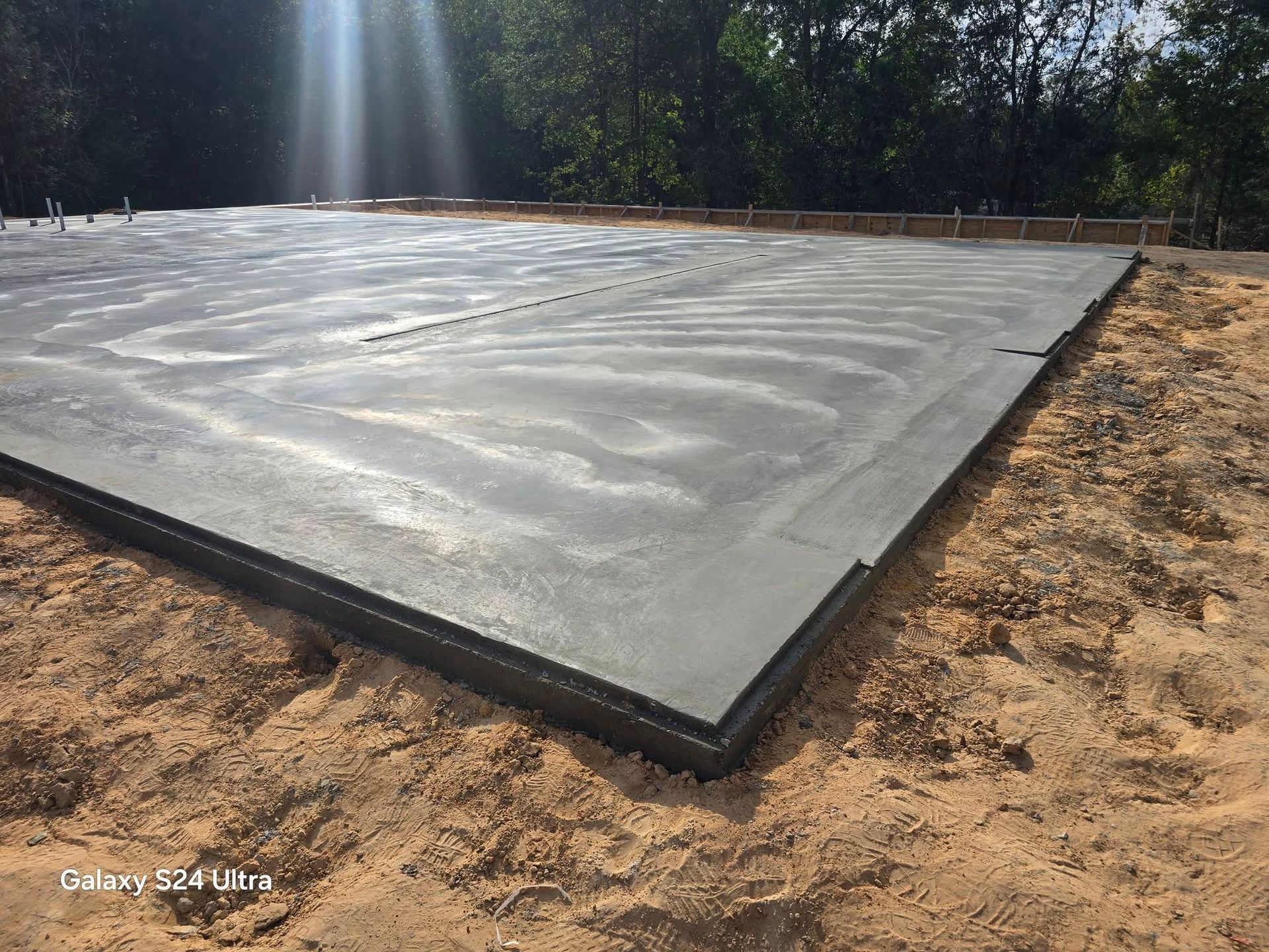 Newly poured concrete foundation with wooden frame, on sandy ground, with sunlight.