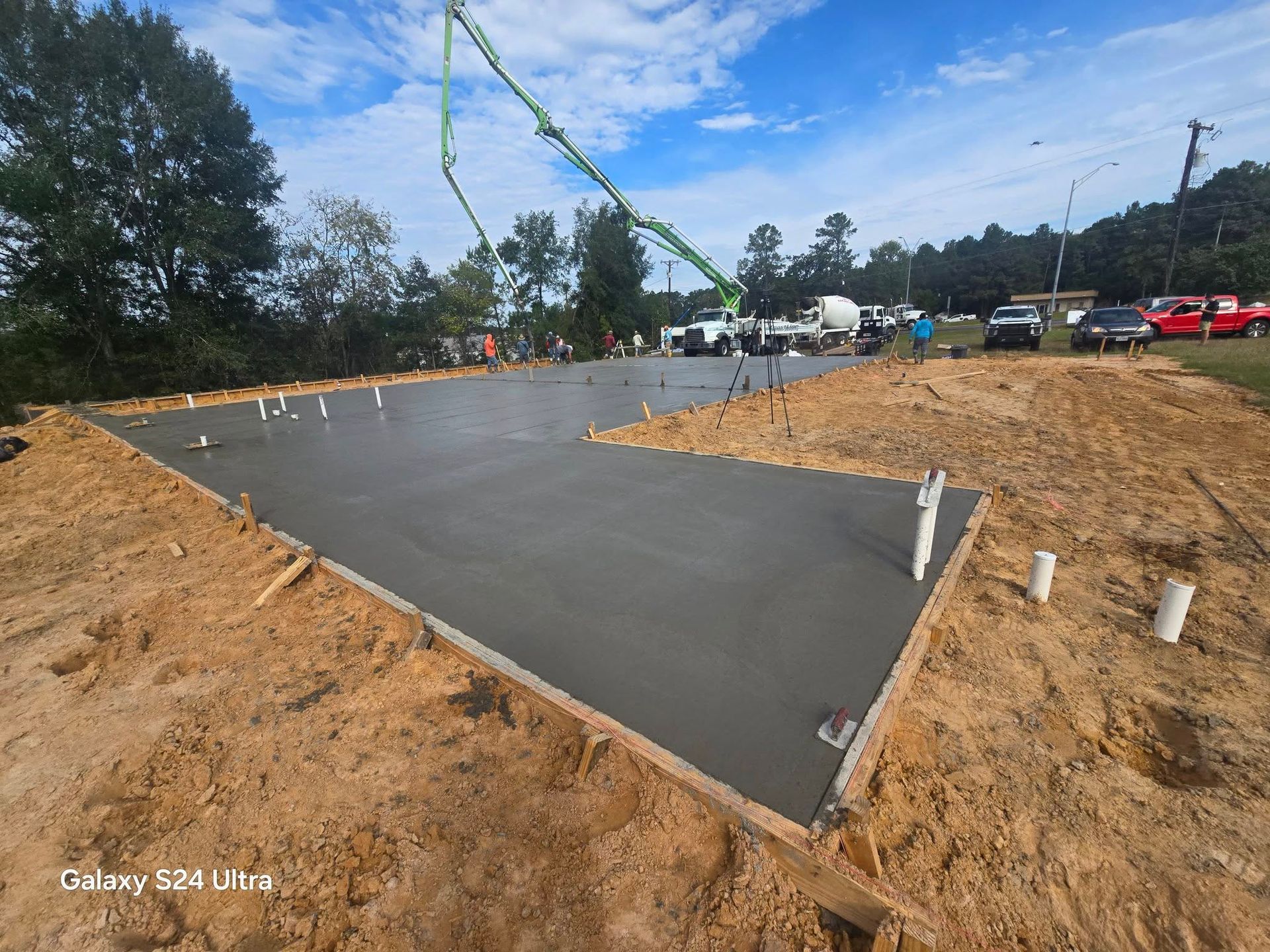 Freshly poured concrete foundation with plumbing pipes and concrete pump in a construction site.