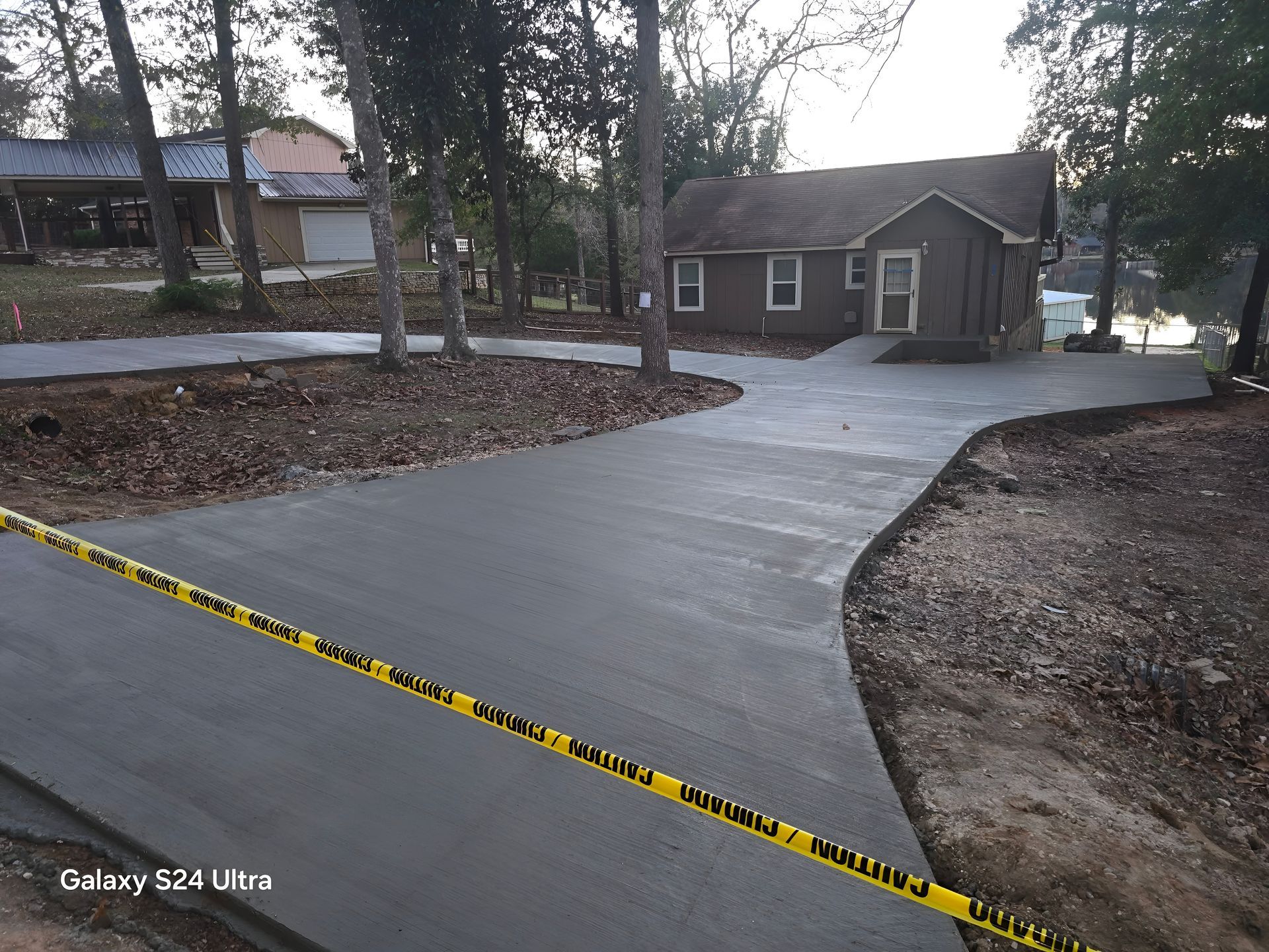 Newly poured concrete driveway leading to a brown house; yellow caution tape in foreground.
