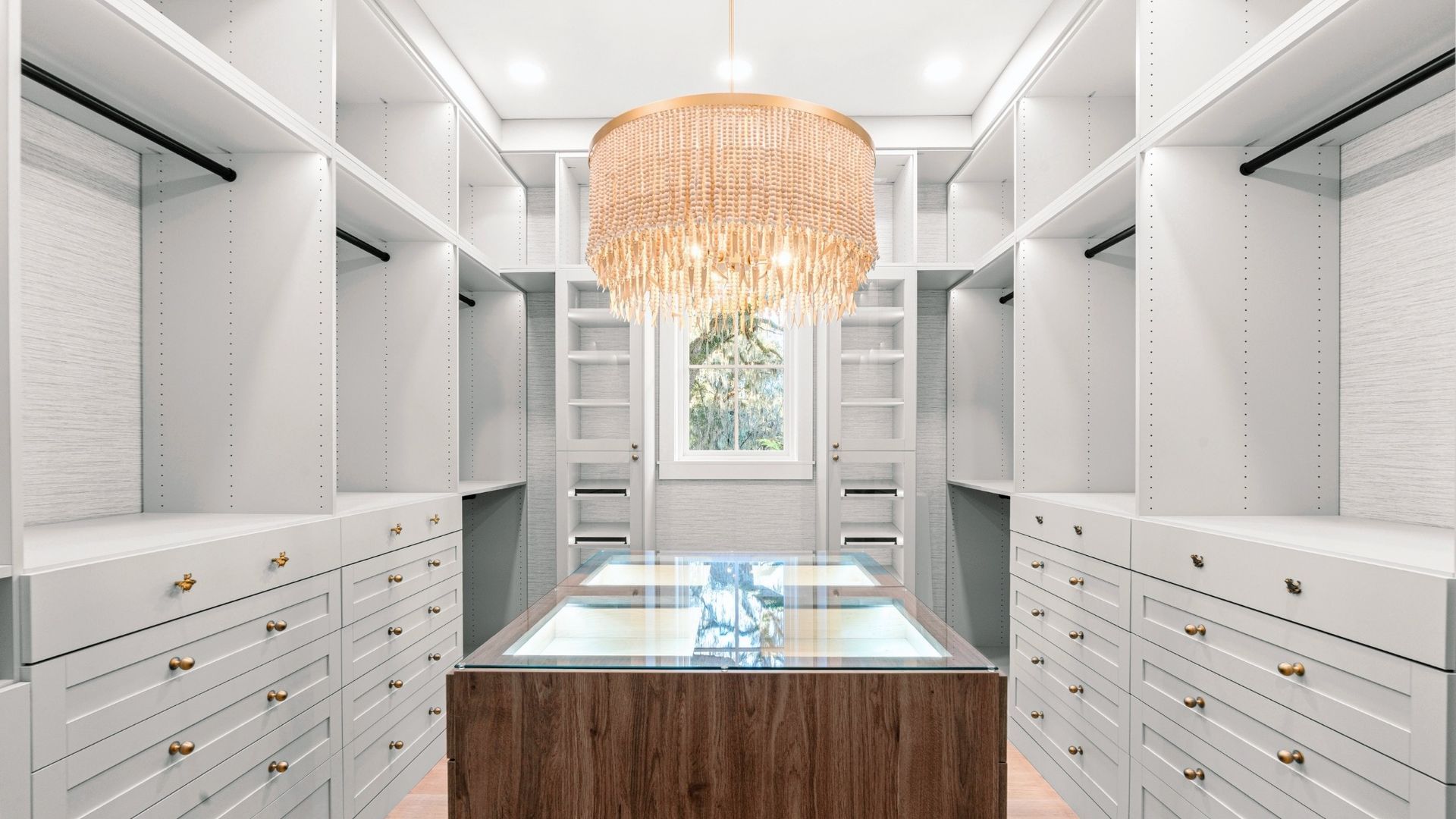 Walk-in closet with white shelves and drawers, a central island, and a decorative chandelier.