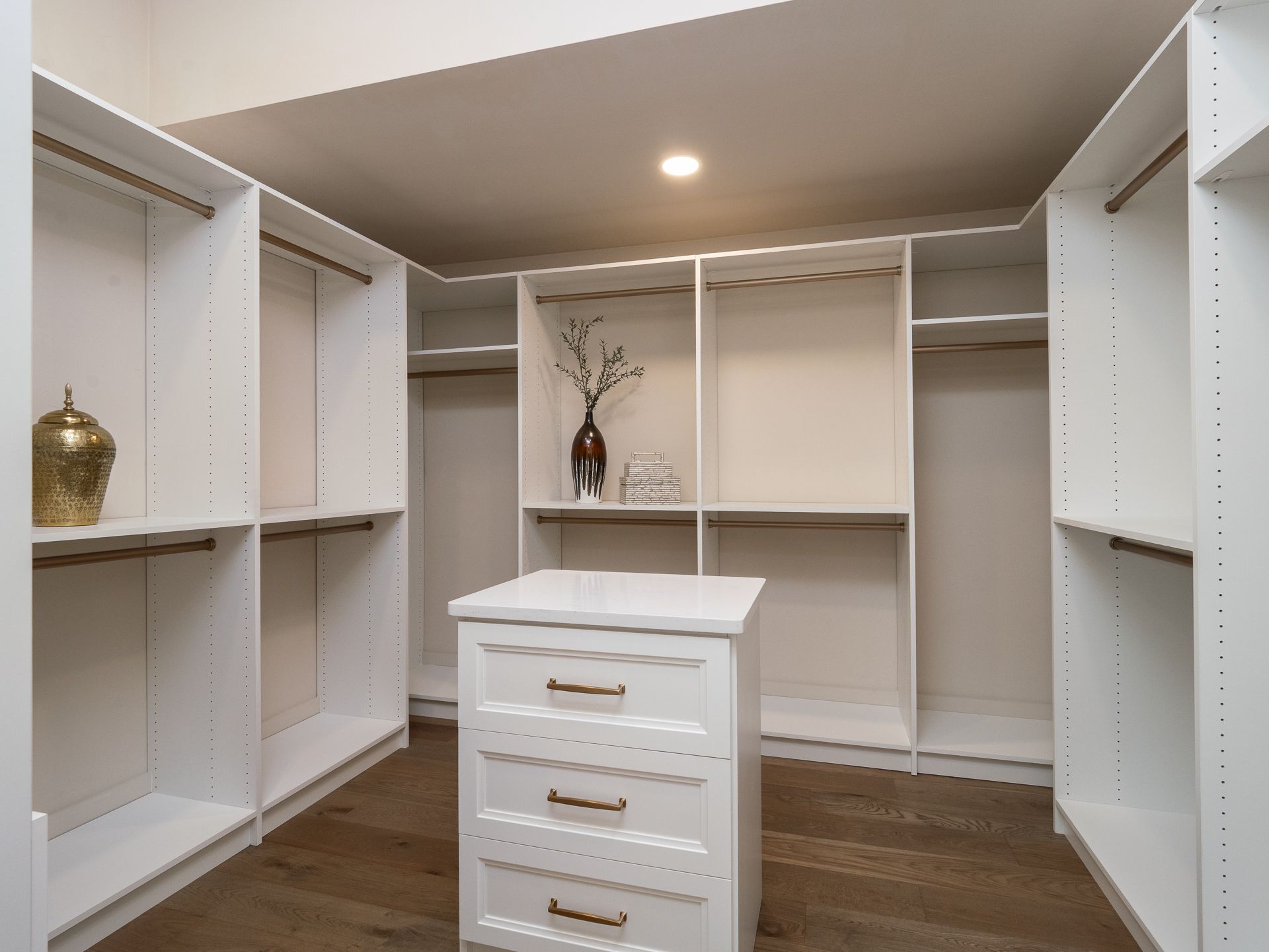 White walk-in closet with shelves and drawers; wooden floor; decorative items.