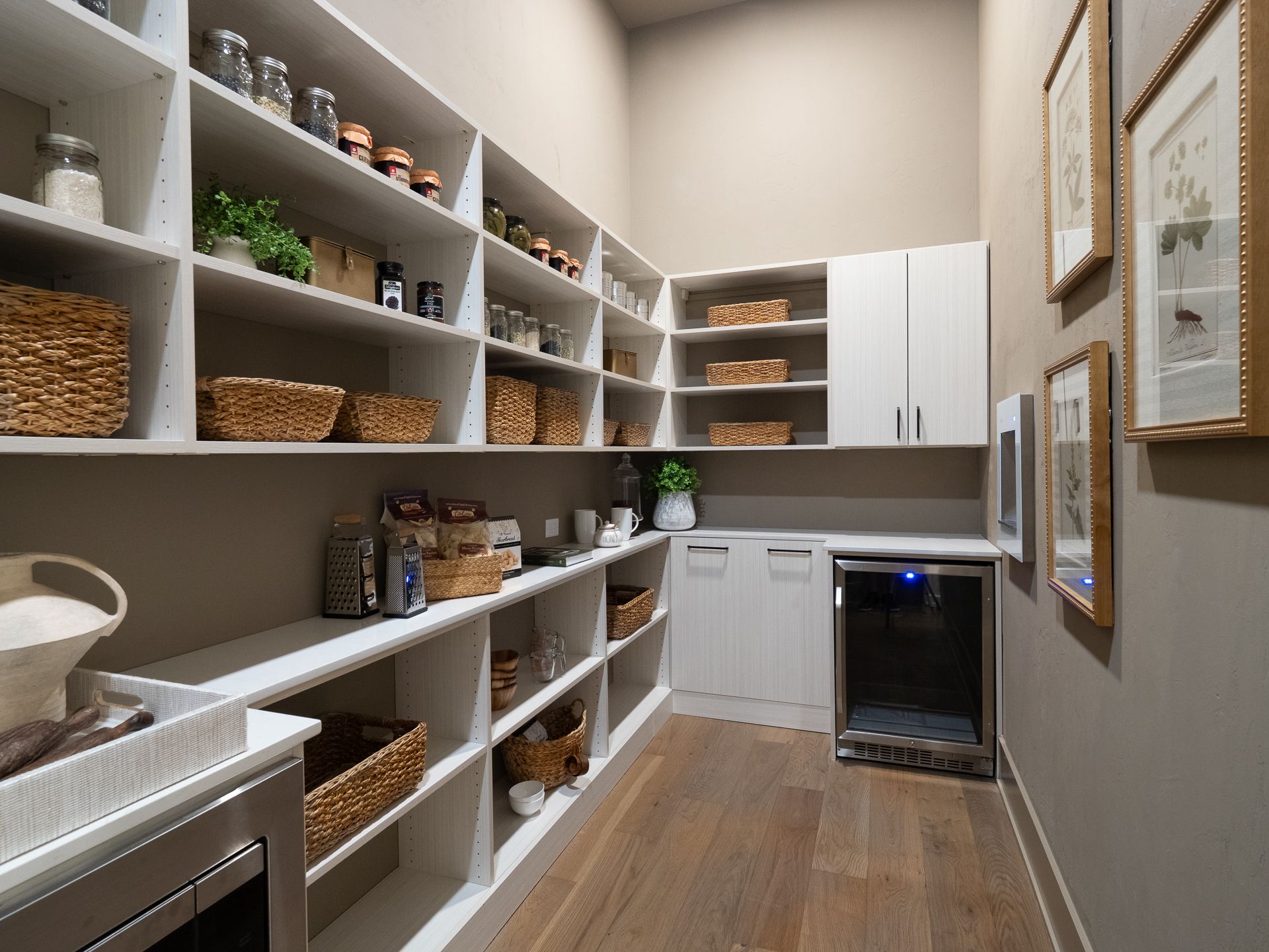 A well-organized pantry with white shelves and various food items and baskets on display. Includes a mini-fridge and cabinets.