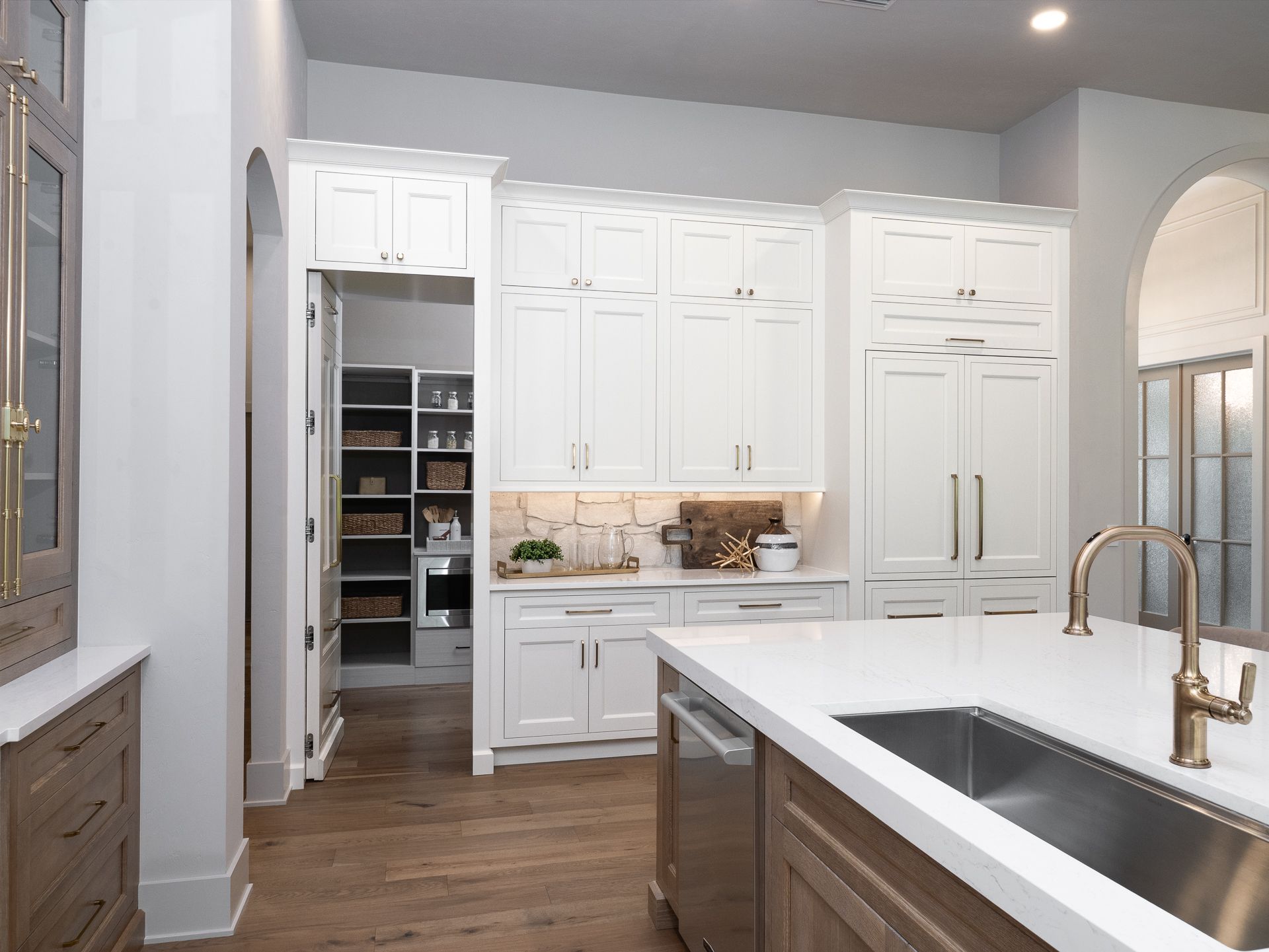 White kitchen with pantry, island, and sink; wood cabinets and floor.