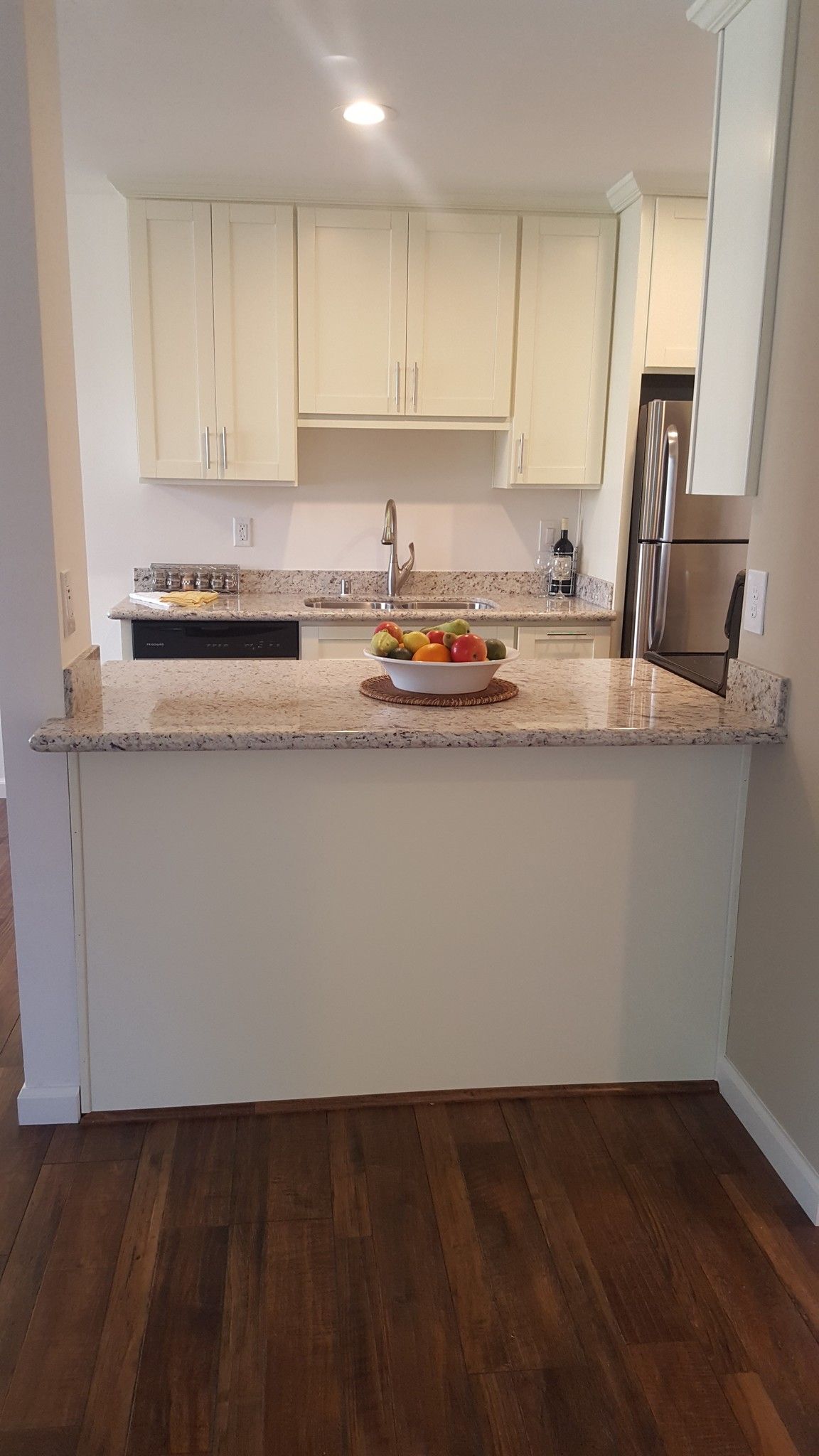 A kitchen with white cabinets , granite counter tops , stainless steel appliances and a bowl of fruit on the counter.